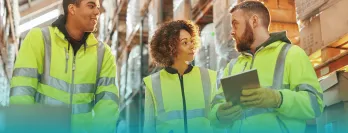 Three people discussing logistics in a warehouse.